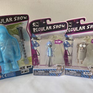 May include: Three Regular Show action figures in their original packaging. The figures include a blue yeti-like character with a sword, Mordecai, and Rigby. The packaging features the show's logo and character names.
