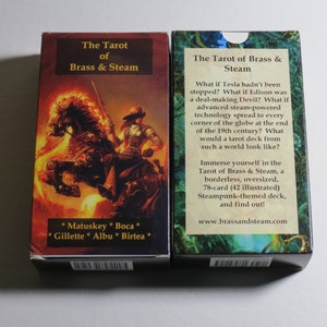 May include: Two boxes of the Tarot of Brass & Steam playing cards. The front of the box on the left shows a steampunk illustration of a rider on a fiery horse. The back of the box on the right shows text describing the deck as a 78-card, oversized, borderless, steampunk-themed deck.