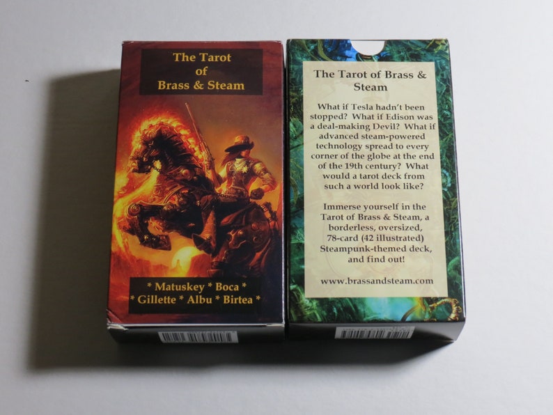 May include: Two boxes of the Tarot of Brass & Steam playing cards. The front of the box on the left shows a steampunk illustration of a rider on a fiery horse. The back of the box on the right shows text describing the deck as a 78-card, oversized, borderless, steampunk-themed deck.