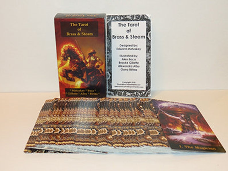 May include: A tarot deck box with the title "The Tarot of Brass & Steam" and a card from the deck showing a steampunk-inspired illustration of a magician. The box is red with gold accents and the card is purple with gold accents.