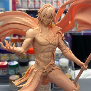 May include: A detailed, unpainted figurine of a male character in a dynamic pose, holding a staff and a flowing cape. The figure has detailed musculature and intricate costume elements. The color is a light peach.
