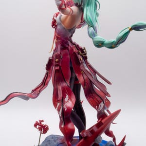 Puede incluir: Figura detallada de un personaje con cabello verde menta fluido y un atuendo rojo y blanco. La figura est&aacute; posada con un brazo levantado, y la base presenta detalles en rojo y un efecto de agua azul.