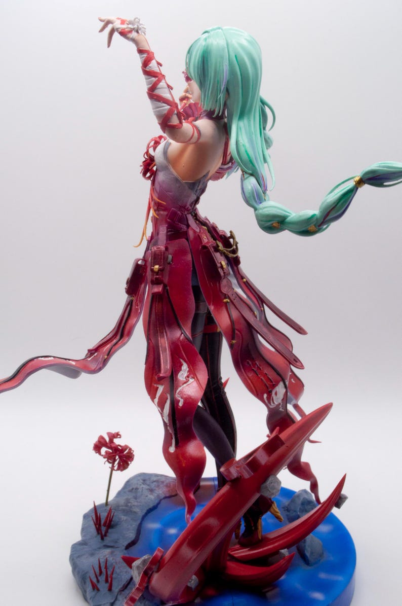 Puede incluir: Figura detallada de un personaje con cabello verde menta fluido y un atuendo rojo y blanco. La figura est&aacute; posada con un brazo levantado, y la base presenta detalles en rojo y un efecto de agua azul.