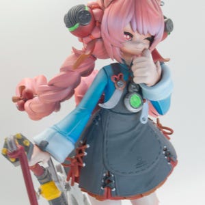 May include: A collectible anime-style figurine featuring a character with pink hair, large ears, and red eyes. The figure wears a blue top, a dark gray apron with lace-up details, and holds a red and white staff with a small white rabbit-like charm.