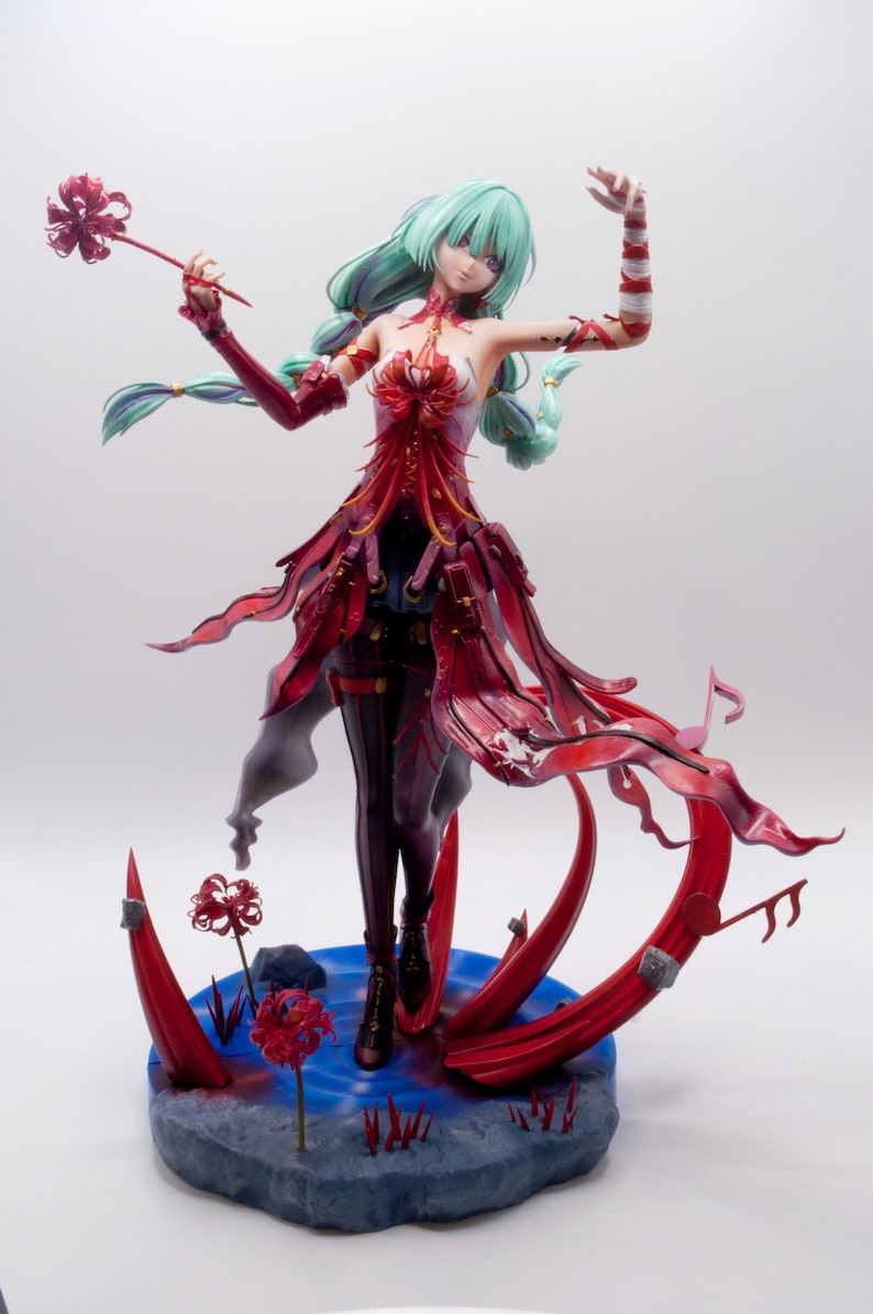 Puede incluir: Figura detallada de una mujer con cabello verde menta y un vestido rojo y negro. La figura est&aacute; posada sobre una base azul con detalles florales rojos. La figura es un objeto de colecci&oacute;n.