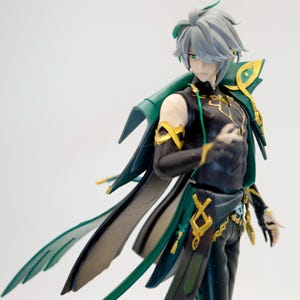 May include: A detailed figurine of a character with gray hair and green eyes, wearing a black and green outfit with gold accents. The figure has a flowing cape and is posed in a dynamic stance.