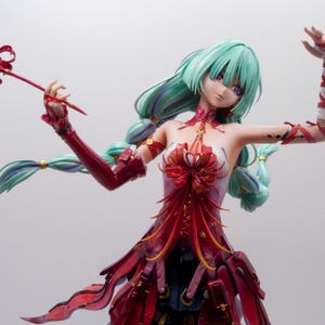 Puede incluir: Figura detallada de un personaje de anime femenino con cabello verde menta y un vestido rojo y blanco. La figura sostiene un objeto rojo en forma de flor y tiene cubiertas rojas para los brazos.