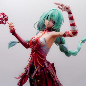 Puede incluir: Figura detallada de una mujer con cabello turquesa y ojos morados, vestida con un vestido rojo y blanco. Sostiene un objeto rojo en forma de flor en una mano y tiene el otro brazo levantado. La figura tiene una pose din&aacute;mica y detalles intrincados.