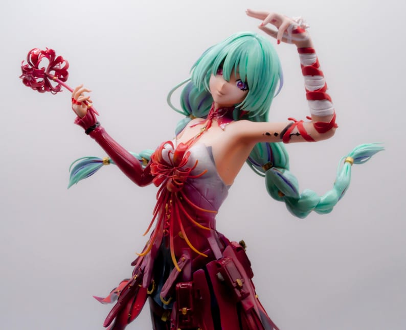 Puede incluir: Figura detallada de una mujer con cabello turquesa y ojos morados, vestida con un vestido rojo y blanco. Sostiene un objeto rojo en forma de flor en una mano y tiene el otro brazo levantado. La figura tiene una pose din&aacute;mica y detalles intrincados.