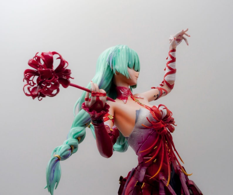 Puede incluir: Figura de una mujer con pelo largo verde claro en una trenza, vestida con un vestido rojo y morado. Sostiene una flor roja en una mano y tiene el otro brazo levantado. La figura tiene un dise&ntilde;o detallado y est&aacute; sobre un fondo liso.