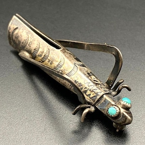 Könnte beinhalten: Ein silberfarbenes Metallobjekt in Insektenform mit türkisfarbenen Augen. Das Objekt hat aufwendige geätzte Details und einen Griff. Das Insekt hat sechs Beine und einen gebogenen Körper. Es ist wahrscheinlich ein dekorativer Gegenstand oder ein kleiner Behälter.