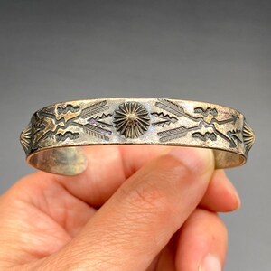 May include: Silver-toned cuff bracelet with etched geometric and arrow designs. The bracelet features a central sunburst motif and decorative end caps. The open cuff design allows for easy wear. A vintage-style piece.