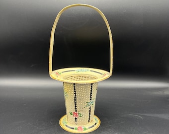 Puede incluir: Una cesta de metal vintage con asa. La cesta es de color crema con un diseño perforado y está decorada con motivos florales en rosa, azul y verde. Rayas verticales negras añaden contraste.