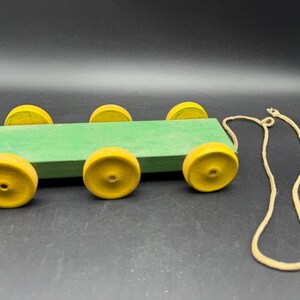 May include: A vintage wooden pull toy featuring a green rectangular body and six yellow wheels. A beige string is attached for pulling. The toy is designed for young children.