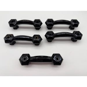 May include: Five black cabinet handles with a curved design and hexagonal ends are arranged on a white surface. The handles have a glossy finish and appear to be made of a durable material. These are likely for furniture.