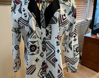 May include: White button-down shirt with a Southwestern geometric pattern in red, green, and gray. The shirt has long sleeves and a black yoke detail. The shirt is displayed on a wicker mannequin.