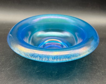 May include: A round, iridescent blue glass bowl with a wide rim. The bowl's interior reflects a spectrum of colors, and the rim has a textured, crackled appearance. The bowl is likely used for decorative purposes.