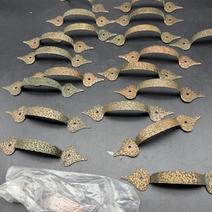 May include: A collection of fifteen metal drawer pulls with a hammered, textured finish and a dark bronze-toned patina. Each pull features a curved handle and two pointed, spade-shaped mounting ends with a single pre-drilled hole in each end.