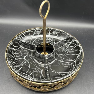 May include: A vintage serving tray with a black interior and white abstract design. The tray is divided into sections and has a gold-colored handle and decorative filigree around the base. A stylish piece for serving snacks.