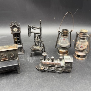 May include: A collection of miniature metal objects, including a grandfather clock, spinning wheel, two lanterns, a piano, and a train. The items are detailed and appear to be antique-style collectibles.