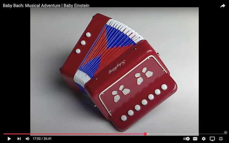 May include: A red toy accordion with white, blue, and red bellows. The accordion has white buttons and a decorative panel with white shapes. The word "Skyfling" is printed on the front.