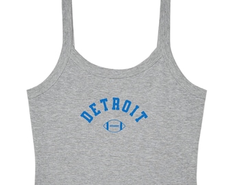 May include: A heather gray sleeveless crop top featuring the word DETROIT printed in a bold blue arched font above a blue graphic illustration of an American football. The garment has a scoop neckline and wide shoulder straps.