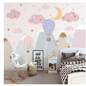 Könnte beinhalten: Eine rosa und blaue Kinderzimmer-Tapete mit einem verspielten Design mit Bergen, Wolken, Sternen und Heißluftballons. Der Text "exist to be happy off to press" ist auf einem schwarzen Rahmen gedruckt.