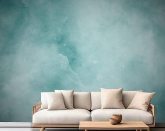Könnte beinhalten: Ein weißes Sofa mit drei Kissen steht vor einer blaugrünen Wand mit Aquarell-Effekt. Das Sofa hat einen Holzrahmen und -beine. Ein Holz-Couchtisch steht vor dem Sofa.