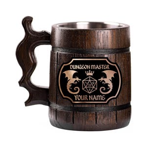 Op de afbeelding: Een donkerbruine houten bierpul met een decoratief handvat. De pul heeft een zwart en goud embleem met de woorden "DUNGEON MASTER" en "YOUR NAME", samen met draken- en dobbelsteenafbeeldingen. De binnenkant is van roestvrij staal.