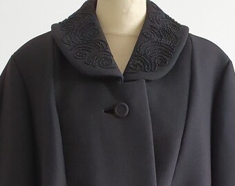 Può includere: Un cappotto nero a maniche lunghe con colletto e polsini rifiniti con ricami neri. Il cappotto ha una chiusura con bottoni.