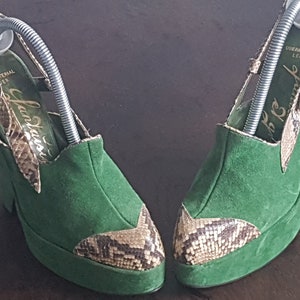Puede incluir: Un par de tacones de plataforma de ante verde con detalles de estampado de serpiente. Los tacones tienen un diseño de tiras en la parte trasera y presentan el texto "Fantasia" en la plantilla. Los zapatos están en buen estado y parecen vintage.