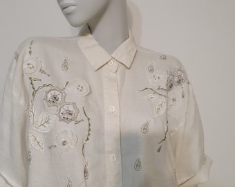 May include: A white button-down shirt with short sleeves and a floral embroidery design in silver and white.