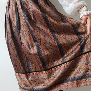 May include: A brown and black patterned skirt with a black velvet trim. The skirt has a vertical striped pattern with a floral design.