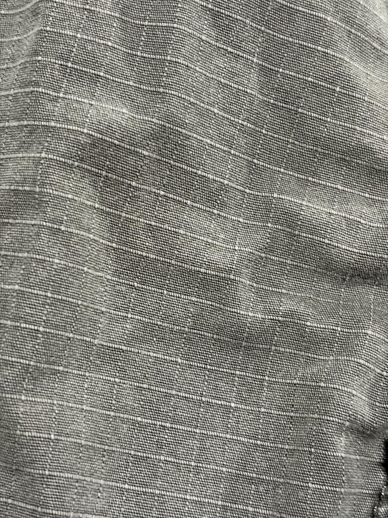Pu&ograve; includere: Primo piano di un tessuto grigio con un motivo a griglia. Il tessuto ha un aspetto strutturato con una sottile lucentezza. La griglia &egrave; formata da sottili linee bianche che si intersecano per creare piccoli quadrati. L'aspetto generale &egrave; pulito e strutturato.