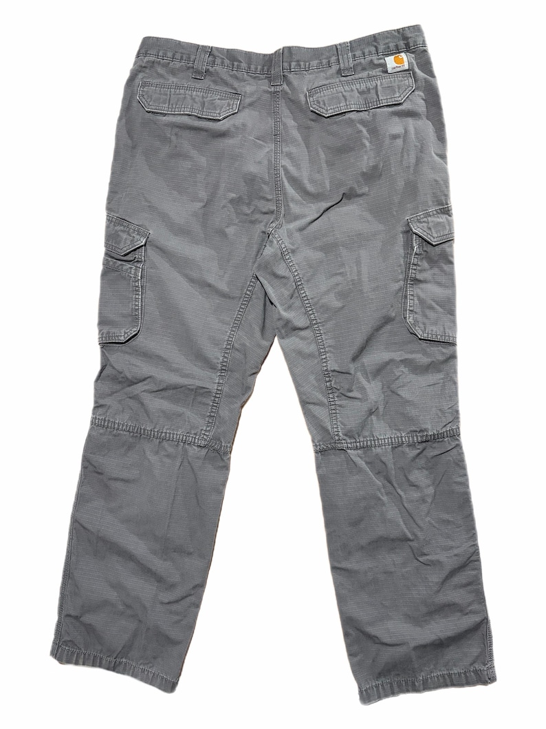 Pu&ograve; includere: Pantaloni cargo grigi con multiple tasche, tra cui due sul retro e due su ogni gamba. I pantaloni hanno una vestibilit&agrave; rilassata e sono realizzati in un tessuto resistente. Il logo Carhartt &egrave; visibile.