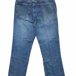May include: Blue denim jeans with a classic five-pocket design. The jeans have a straight leg cut and a faded wash. A leather patch with text is visible on the back waistband.