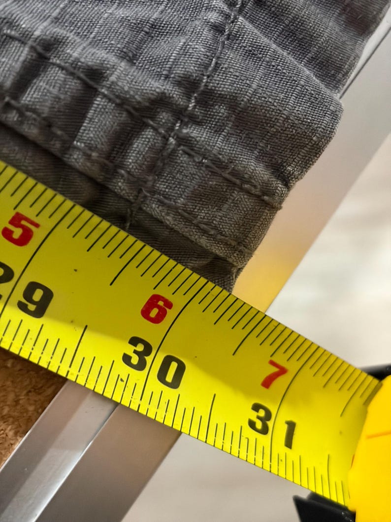 Pu&ograve; includere: Primo piano di tessuto grigio con cuciture visibili. Un metro a nastro giallo mostra una misura di 76 cm. Il tessuto sembra far parte di un capo di abbigliamento, possibilmente pantaloni o pantaloncini.