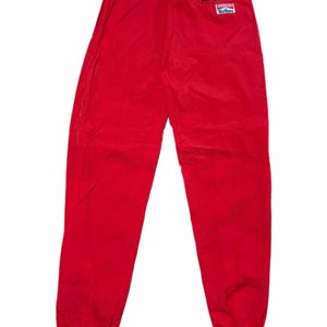 Puede incluir: Pantalones deportivos de color rojo brillante con cintura elástica y puños en los tobillos. Un pequeño parche rectangular con el logotipo de Marlboro está en la parte trasera. Los pantalones están hechos de un material ligero.