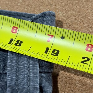 Pu&ograve; includere: Primo piano di un tessuto grigio con un metro a nastro giallo. Il nastro mostra misure da 15,2 a 20,3 cm. Il tessuto sembra essere tessuto.