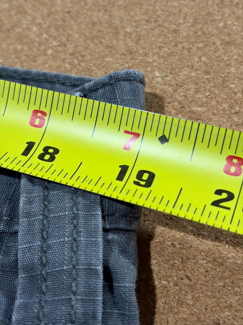 Pu&ograve; includere: Primo piano di un tessuto grigio con un metro a nastro giallo. Il nastro mostra misure da 15,2 a 20,3 cm. Il tessuto sembra essere tessuto.