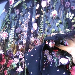 May include: Black sheer fabric with floral embroidery in pink, white, and purple. The embroidery includes detailed flowers and leaves. A dark blue garment with white polka dots and floral beadwork is also visible.