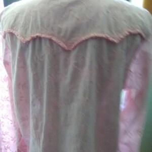 May include: A light pink button-down shirt with a floral pattern. The yoke and collar are a lighter shade of pink, trimmed with a scalloped edge. The shirt has long sleeves and a classic collar.