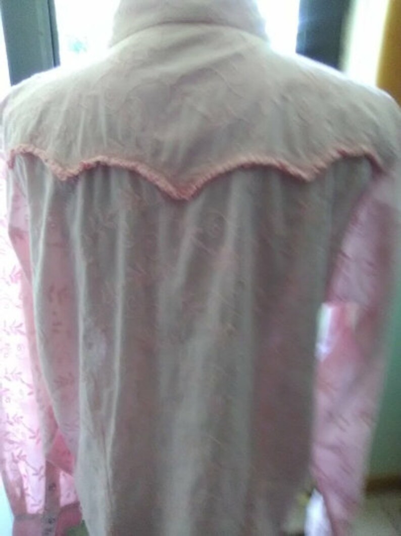 May include: A light pink button-down shirt with a floral pattern. The yoke and collar are a lighter shade of pink, trimmed with a scalloped edge. The shirt has long sleeves and a classic collar.