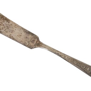 May include: A vintage silver butter knife with an ornate design on the handle. The knife has a slightly tarnished finish.