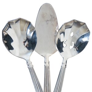 May include: Three silver serving spoons with fluted handles. The spoons have different shapes, including a round spoon, a slotted spoon, and a flat serving spoon.