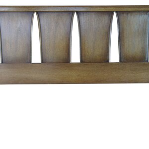 May include: A wooden headboard with a mid-century modern design. The headboard has a rectangular shape with a solid wood panel and a decorative top section with five vertical, slightly curved panels.