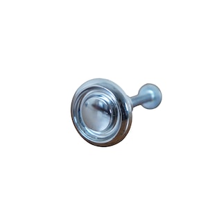 May include: A silver knob with a round, slightly raised center and three concentric circles around it. The knob is attached to a short, silver post.