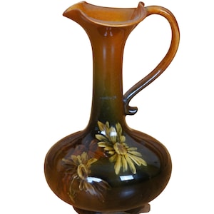 May include: A brown ceramic pitcher with a wide mouth and a curved handle. The pitcher is decorated with a floral design in shades of yellow and brown.