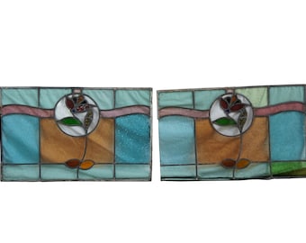 May include: A pair of stained glass windows with a floral design. The windows are made of clear, blue, green, pink, and brown glass. The floral design is in the center of each window and features a red, brown, and yellow flower.