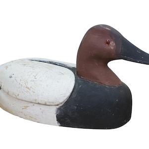 May include: A wooden duck decoy with a white body, black and brown accents, and a black beak. The decoy has a weathered appearance, suggesting it is vintage or antique. The duck is a decorative item.